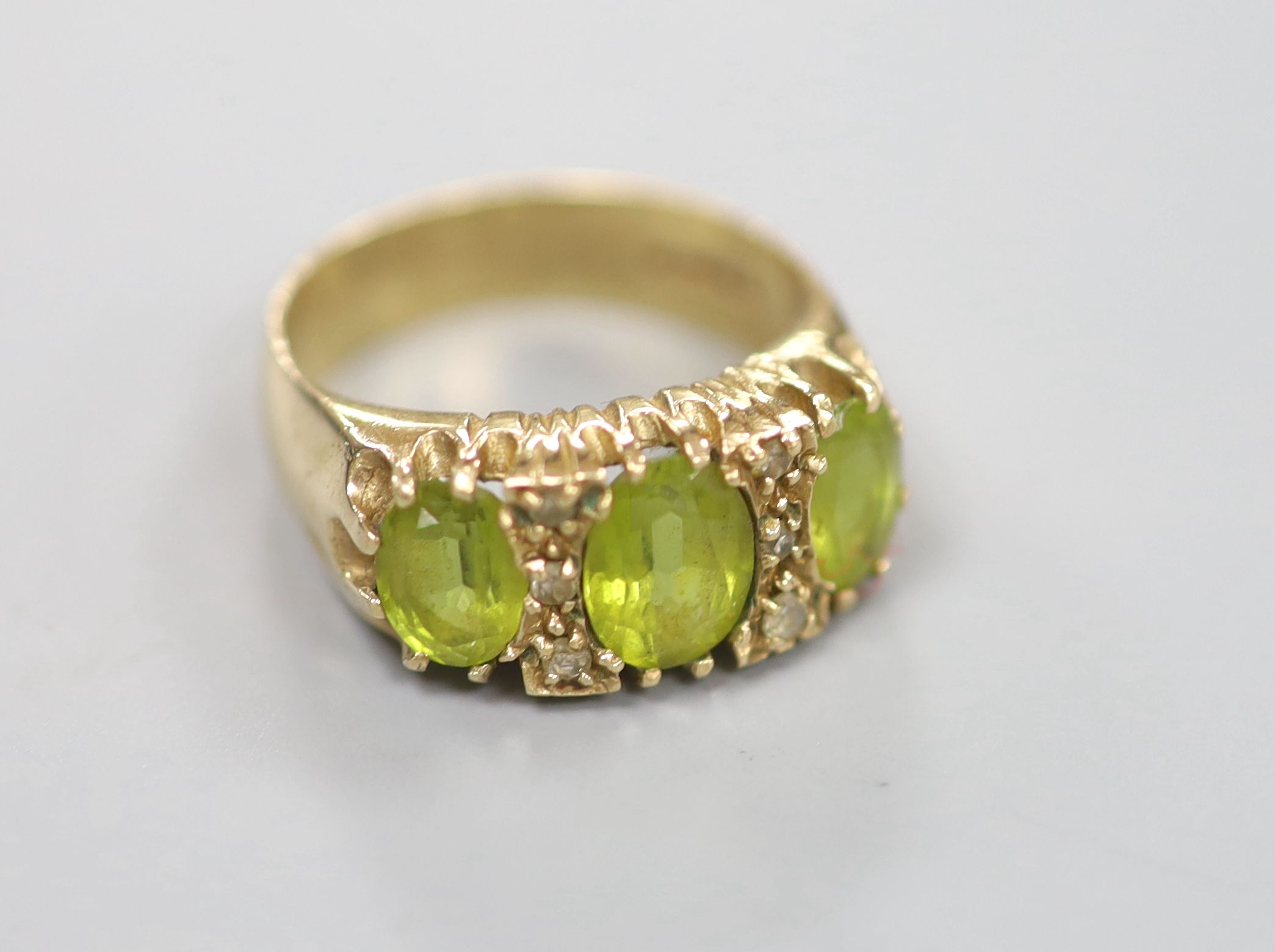 A modern 9ct gold, three stone peridot and diamond chip set dress ring, size P, gross 6 grams.